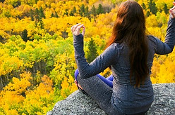 girl sits on rock and meditates over fall foliage and mountain view
