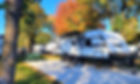 RV that is for rent on a paved campsite under the trees.