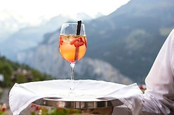 An upscale waiter serving a cocktail in a wine glass with a mountain view in the background