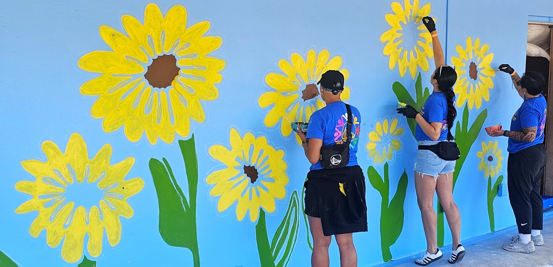 Volunteers painting large yellow flowers on a blue background