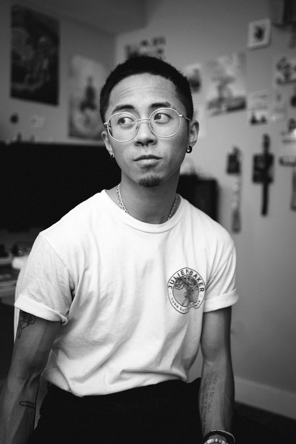 A black & white photograph of Cal at home, sitting down wearing a white t-shirt and round glasses, looking to the right.