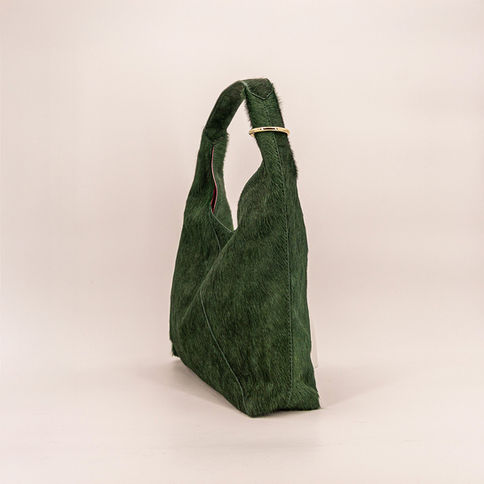 Bundle Bag Pine/Forest Green: Grüne Kuhfell-Tasche mit rosa Innenfutter und Messingring am Henkel.