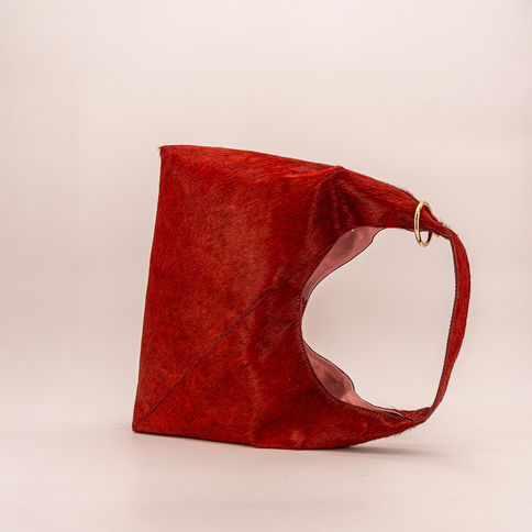 Bundle Bag Bordeaux Red: Bordeauxrote Kuhfell-Tasche mit rosa Futter und Messingring am Henkel.