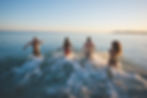 two men and two women running into an ocean at sunset