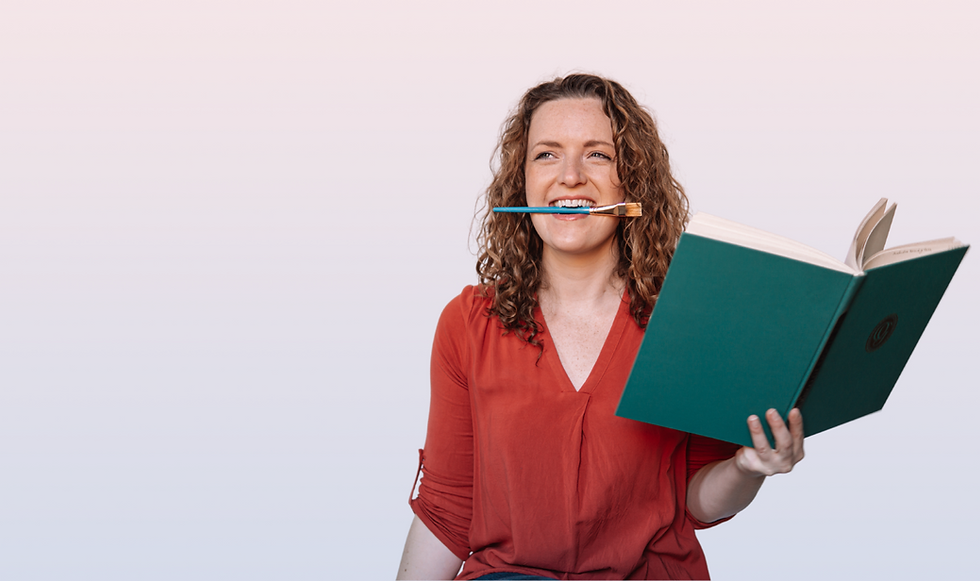 Victoria Hines in a red shirt with a green book and paintbrush in her mouth.