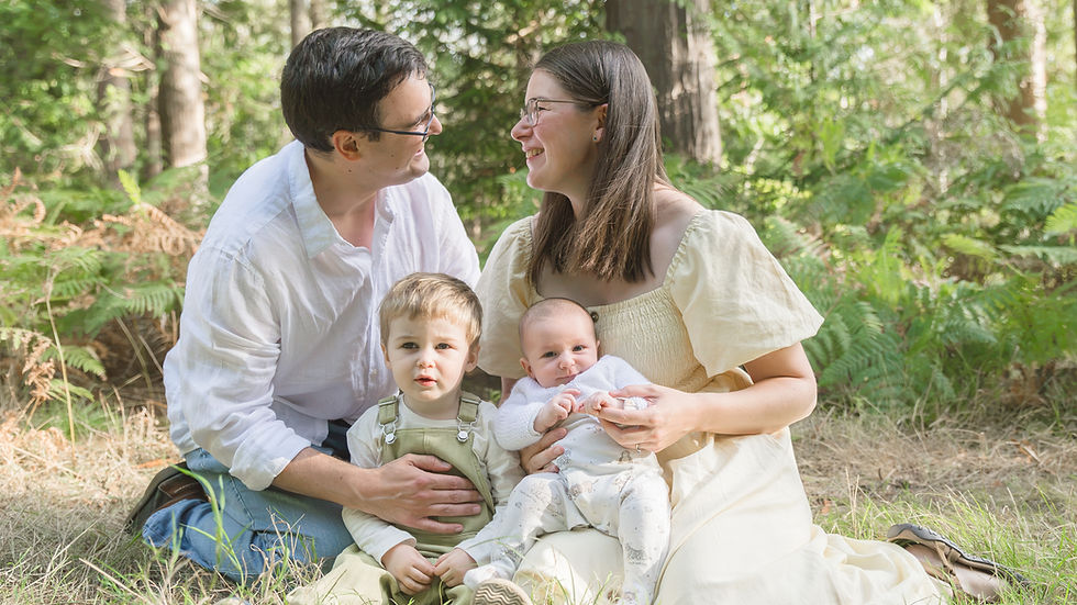 A warm and loving family portrait taken in the serene embrace of a lush forest, capturing a joyful moment between parents and their young children.