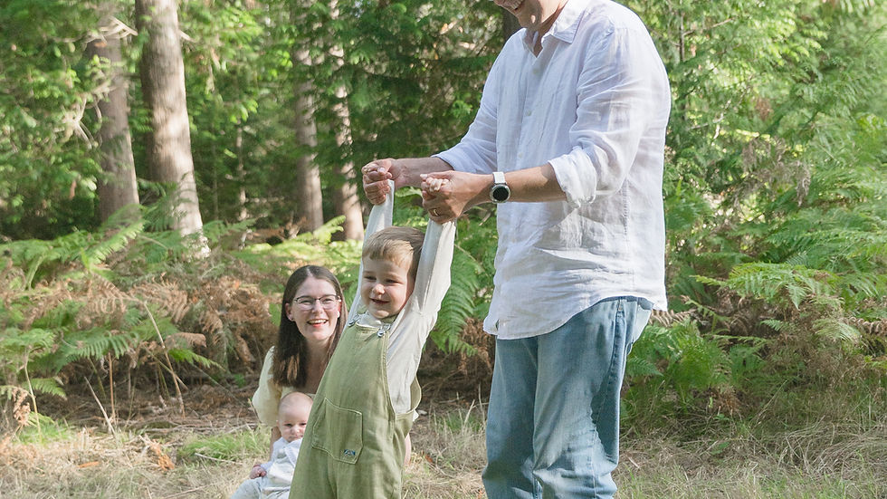 A joyful family moment captured in the woods, with a child playfully swinging between parents as they enjoy a sunny day together.