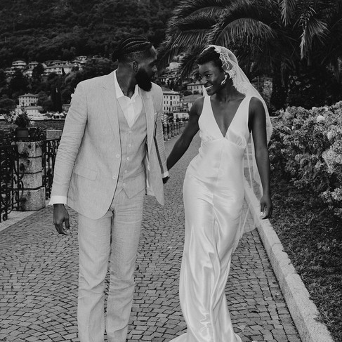 Bride wearing an embroidered mantilla veil walks hand-in-hand with her groom along the cobbled streets of Lake Como.