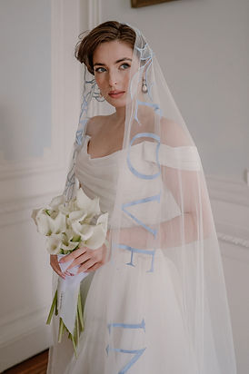 Bride holding white calla lilies and wearing a mantilla wedding veil embroidered with bold blue lettering, offering a modern twist on a classic bridal veil.