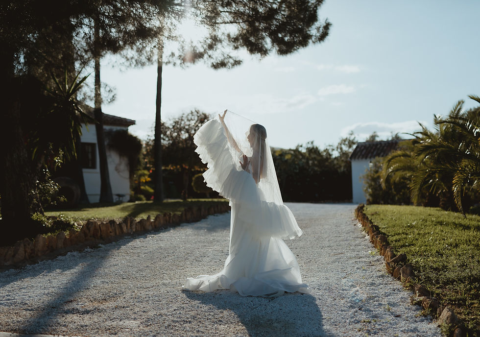 Bride lifting a dramatic ruffled tulle wedding veil in sunlight — statement style from the 2026 bridal veil trends.