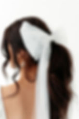 Bride wearing tulle bridal hair bow with long veil tails, modern wedding veil alternative styled in ponytail