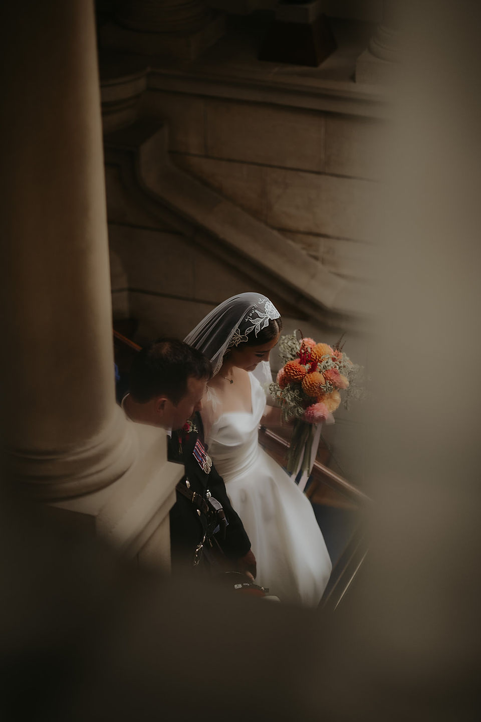 Bride in mantilla veil walking with groom in uniform at BRNC Dartmouth, holding bright bridal bouquet.