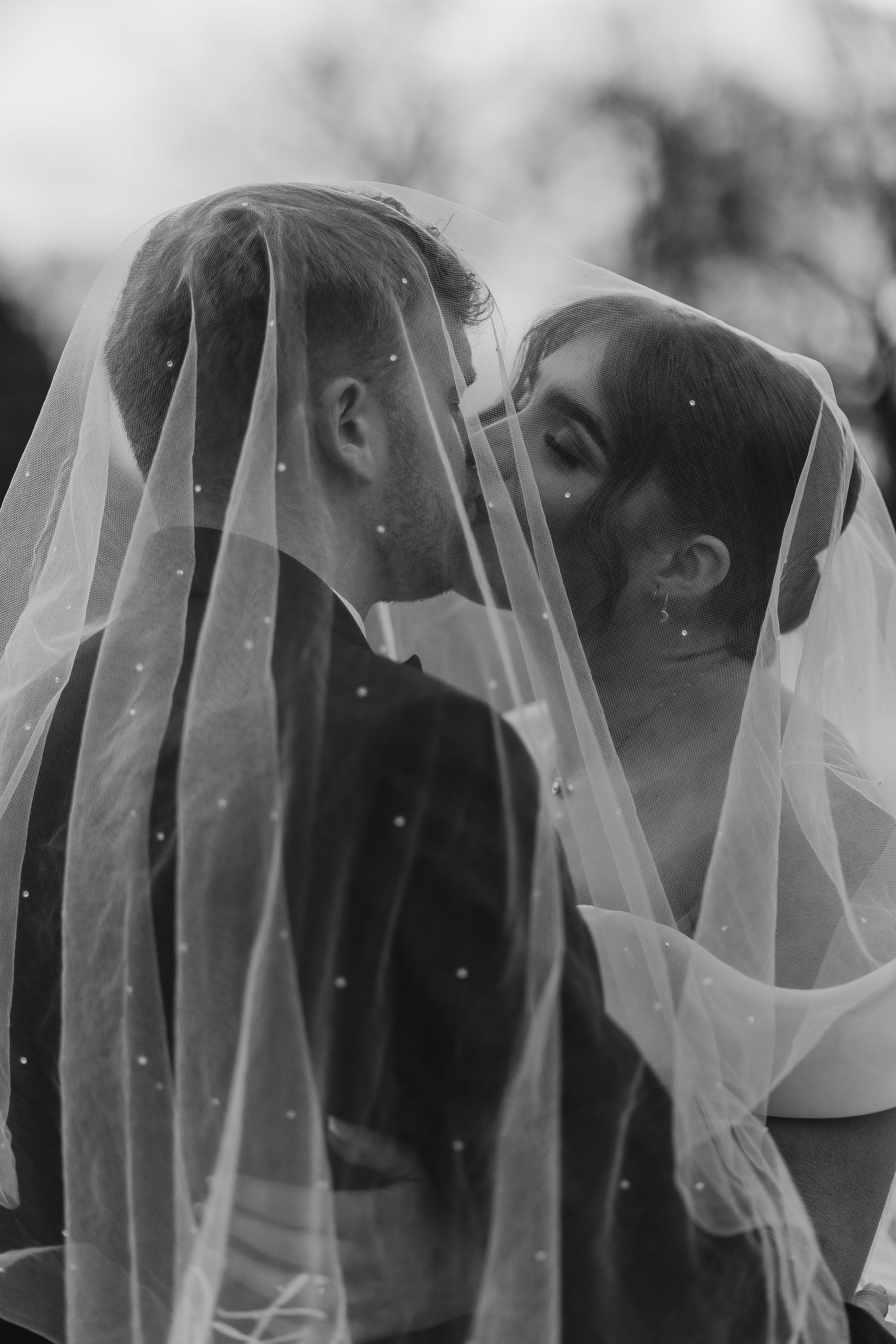 Black-and-white portrait of a couple kissing under the Stardust veil, the shimmering crystals catching light for a timeless, ethereal effect.
