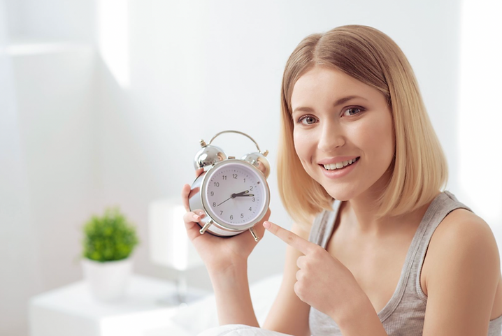 Smiling woman holding an alarm clock, symbolizing the timing aspect of gender swaying methods.