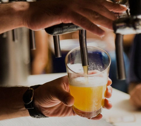 Bartender pouring a fresh beer from a tap into a glass.
