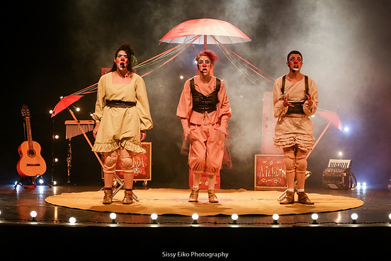Três artistas do Circo di SóLadies em cena no espetáculo A Tenda, com figurinos circenses e guarda-chuvas no palco