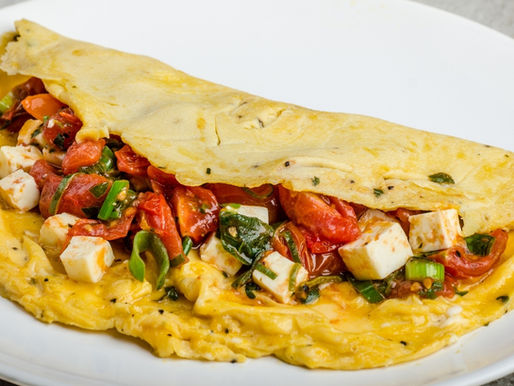 Sirtfood omelet with spinach, chopped tomatoes, and feta cheese, cooked and folded on a plate.