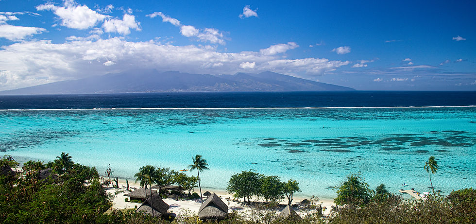 Bright turquoise waters out to dark blue with the island of Tahiti in the background. Palm trees and huts on the sand