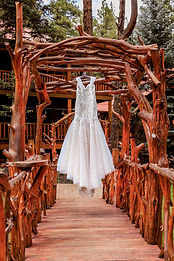 Wedding dress hanging from a rustic wooden arbor above a bridge