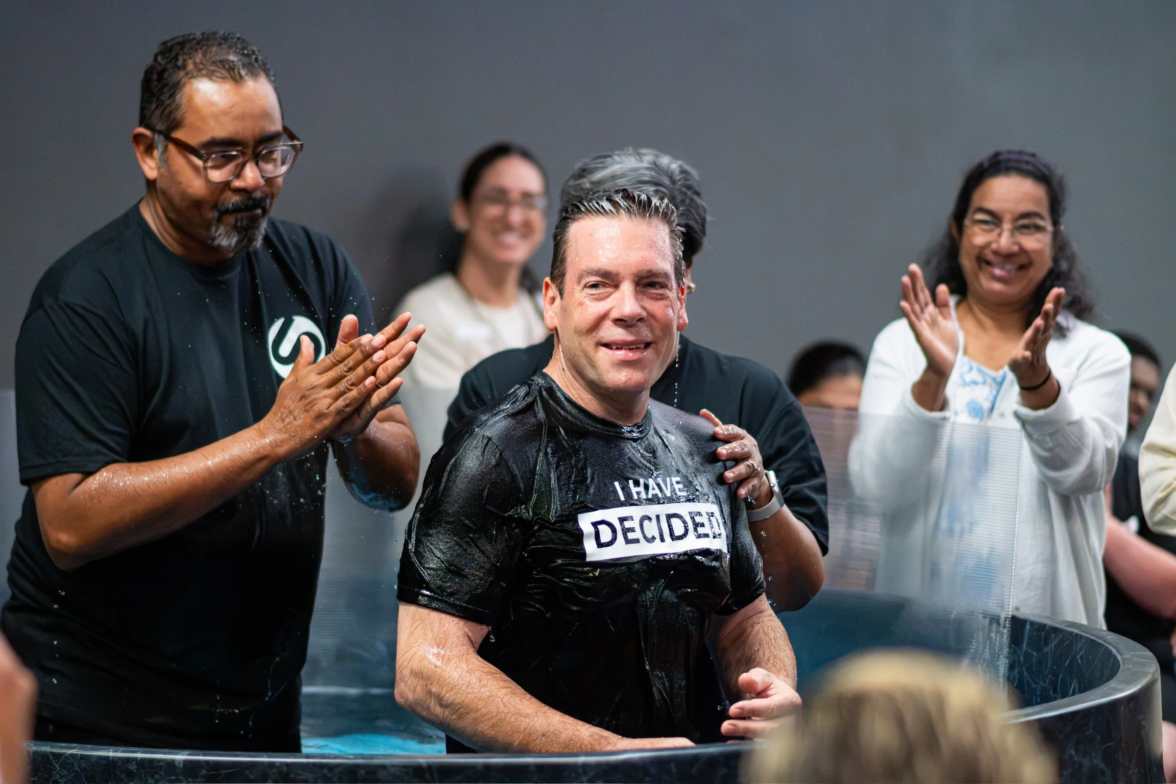 A newly baptized man standing in the pool with ministry support around him