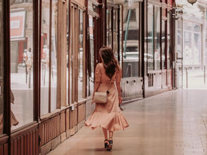 Woman walks away, down a Paris passage hallway in a champagne colored dress, looking into the windows of boutiques. Image credit: Harry Garlick, HG Shoots, 2023
