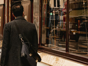 A person in a dark coat and messenger bag walks past a shop with cane displays. Reflections seen in windows. Sign reads "James Smith & Sons."