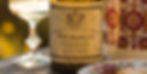 Wine bottle of Bourgogne Chardonnay with ornate label next to a decorative patterned cup and an empty glass, set on a wooden table.