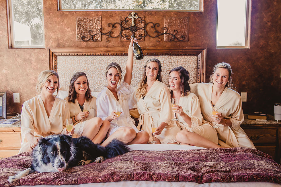 Bridal party popping champagne on bed with cute dog