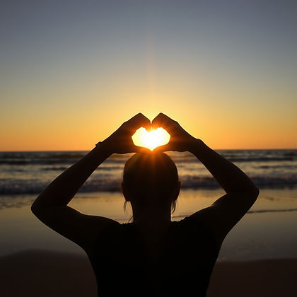 silhouette of person making heart shape with their hands and the sun shining through their