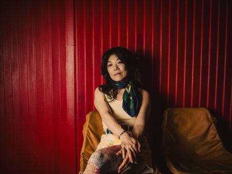 A woman with a neck scarf sitting in a chair in front of a red barn