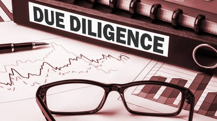 Due diligence binder, eyeglasses, pen, and financial charts on a desk, suggesting careful review.