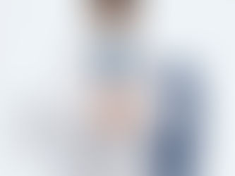 Doctor in a white coat and mask stands thoughtfully, hands clasped.