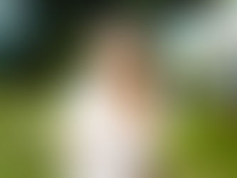 Young woman in a pink sweater stands outdoors, arms crossed, looking pensive. Illustrating not feeling good enough