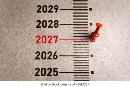Years 2025-2029 on a timeline, with a red pin marking 2027. The numbers are bold, creating a focused and anticipatory mood.