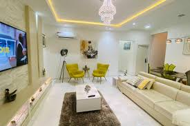 Modern living room with cream sofa, yellow chairs, and chandelier. A shortlet
