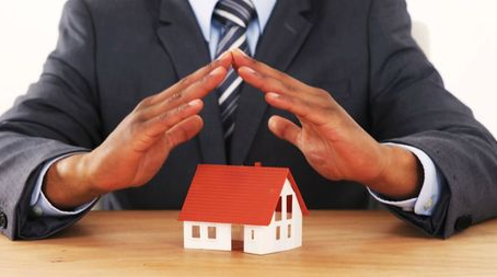 Hands forming a protective gesture over a small model house on a table. Illustrating mortgage