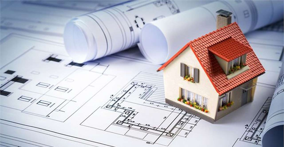 Miniature house model on architectural blueprints with rolled plans, suggesting home design or construction planning.