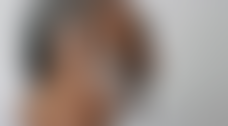 Elderly man with a hearing aid smiles, showing profile. He has gray hair and beard, wearing a white shirt. Light gray background.