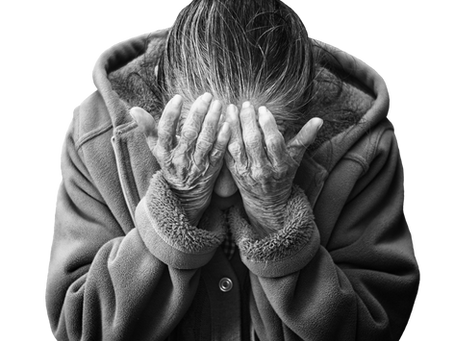 Elderly person in a hoodie covers face with hands, expressing helplessness