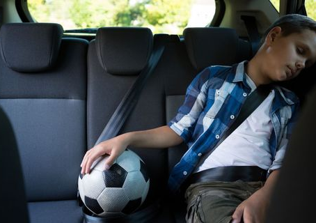Sleeping boy in the back seat of a car, leaning on the window beside a soccer ball, with a calm, tired mood