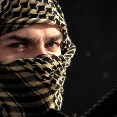 A person wearing a patterned keffiyeh with intense eyes holds a rifle. Illustrating middle East Crisis