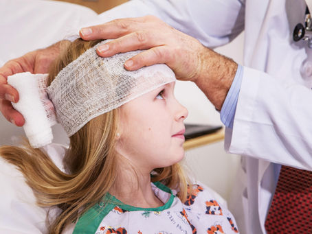 Child with head bandage, assisted by a doctor in a white coat. Illustrating brain injury.
