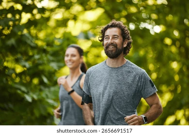 Man and woman jogging in a lush green park, smiling and wearing gray sportswear. Illustrating wellness.