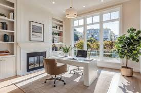Bright home office with a large window, white desk, brown chair, potted plant, shelves, and wall art. Cozy and modern atmosphere.