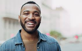 Smiling person outdoors, wearing a denim jacket and brown shirt, illustrating someone in diaspora.