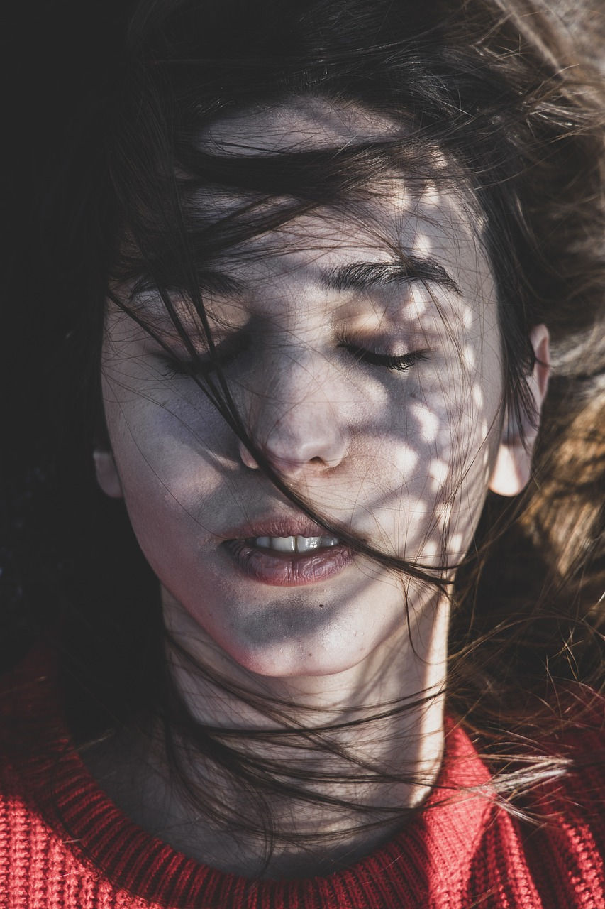 Woman with closed eyes in a red sweater, hair windswept, suggesting emotional resilience