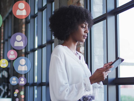 Woman in white blouse looks at phone by a window, surrounded by colorful icons of people. Illustrating social media anxiety.