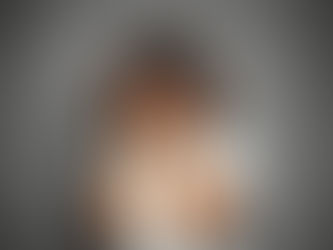 Young girl in a white shirt holds her head in her hands, conveying stress or sadness against a plain gray background.