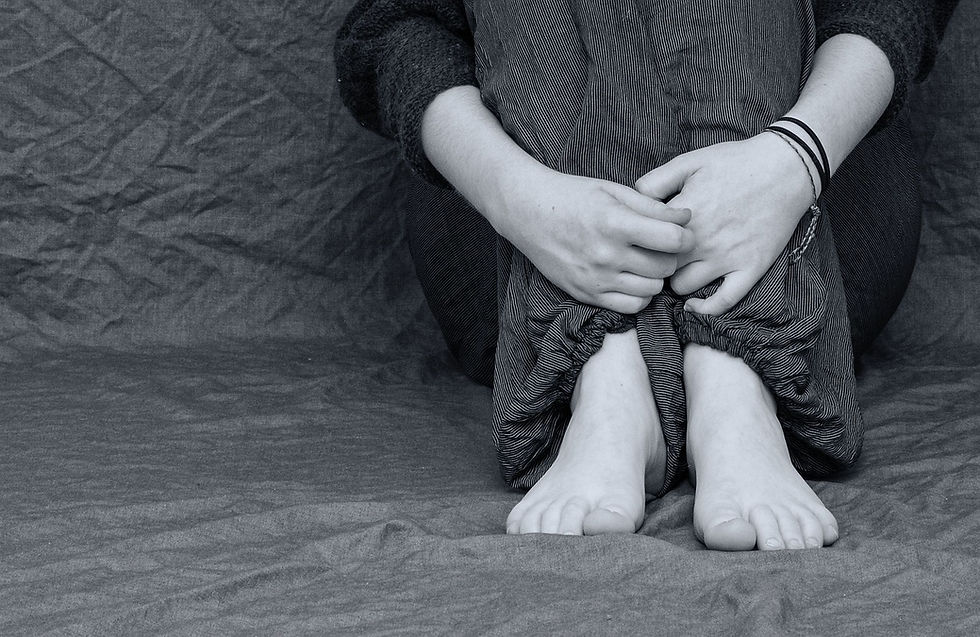 Person sitting with knees drawn up, arms wrapped around legs. Suggesting that they just experienced a loss.