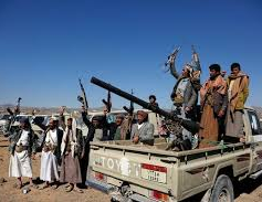 Men in traditional attire raise rifles, standing in a truck under a clear blue sky. Desert background, displaying a tense, defiant mood. Illustrating Yemen Haouthi Strikes.